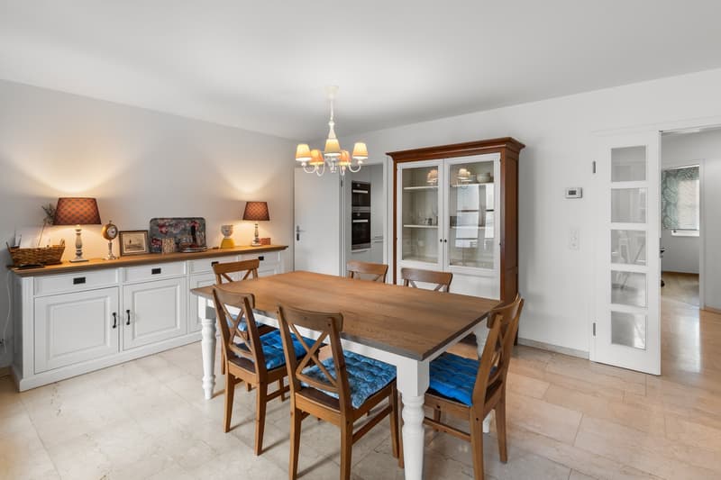White cabinetry, wooden dining table, blue cushioned chairs, wooden floor, chandelier, cabinets with glass doors, wall mounted lamps