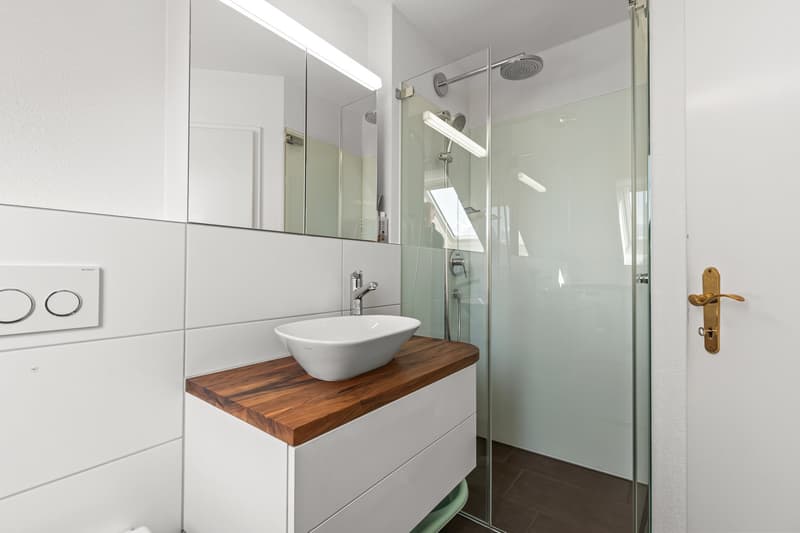 modern bathroom with white tiles, wooden countertop, white sink, glass shower enclosure, shower head, mirror