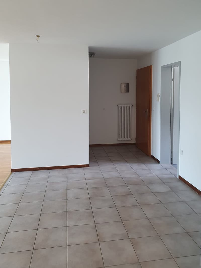 Empty room with white walls, tiled floor, white radiator, wooden door, and power outlets