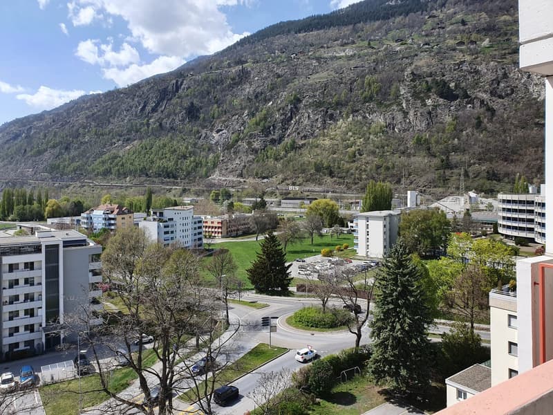 Aerial view of a neighborhood with multiple buildings, a road, and a mountain in the background.