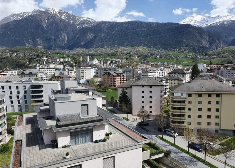 Aerial view of a modern building complex with multiple buildings, surrounded by a green park and mountains in the background.