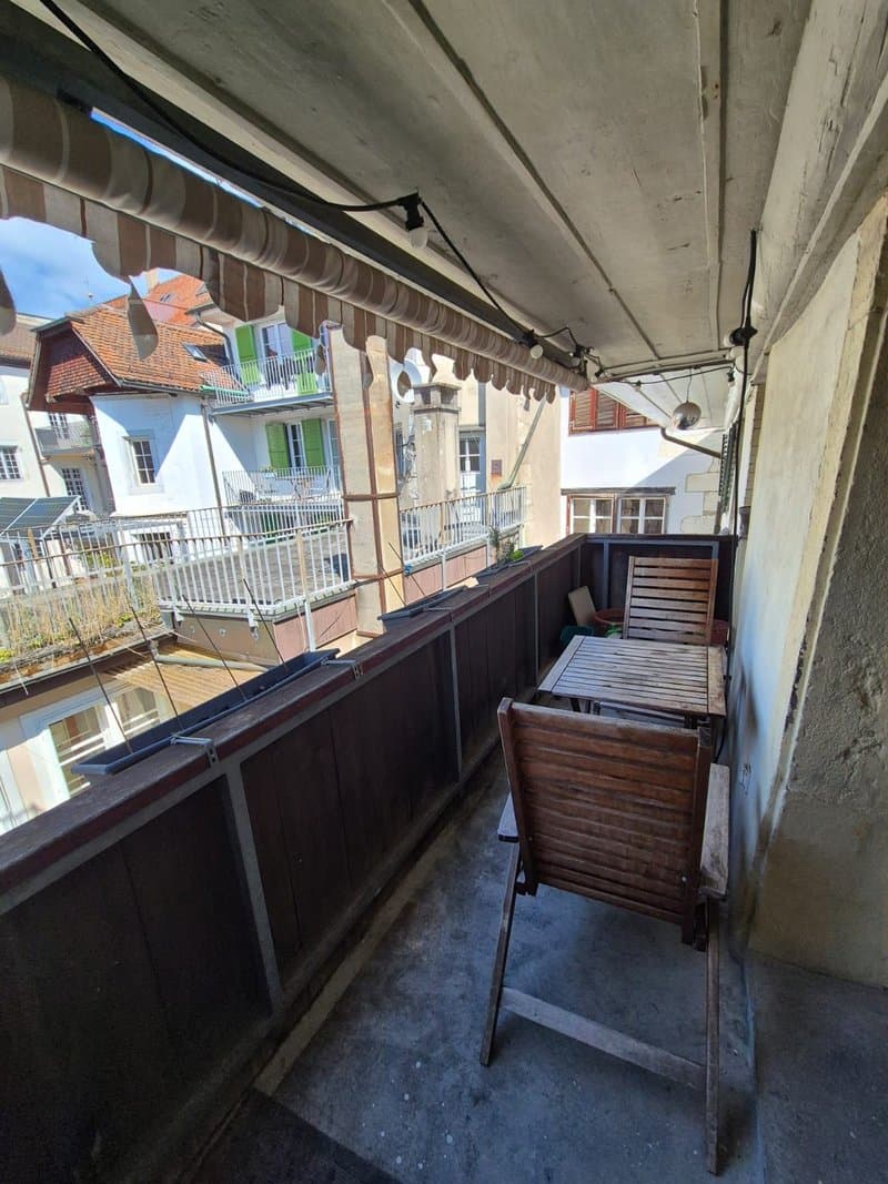 Concrete balcony with wooden furniture, overlooking a residential neighborhood with colorful buildings