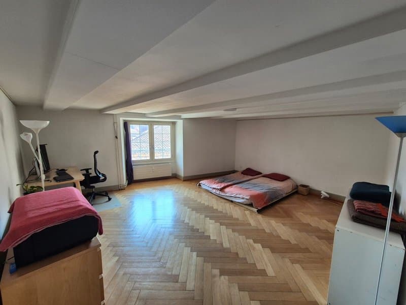 Spacious bedroom with hardwood herringbone flooring, white walls, large windows, two beds, and exercise equipment