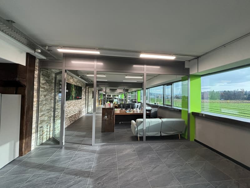 office space with large windows, gray tiled floor, glass doors, wooden desk, white couch, brick wall, green accent wall