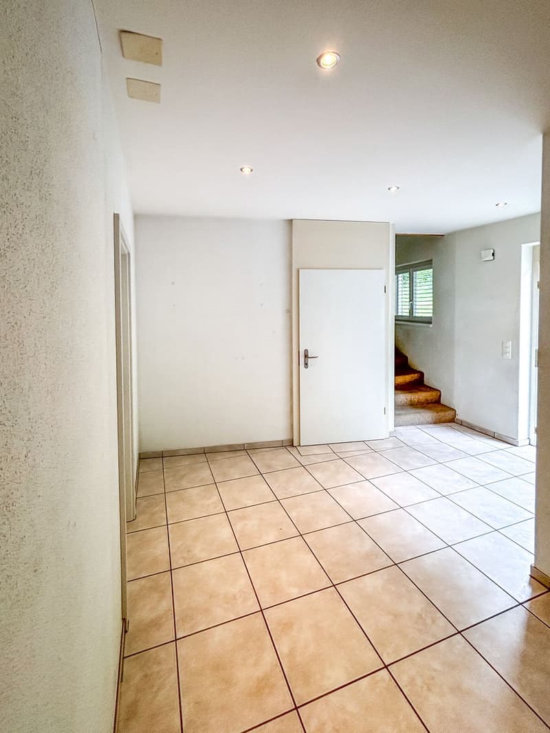 Empty room with tiled floor, white walls, white door, and a staircase leading to the upper floor.
