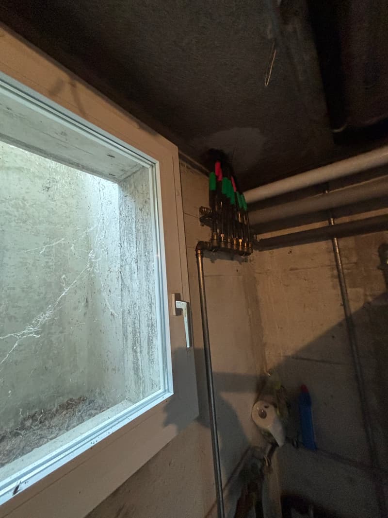 A small room with a window, pipes, and tools hanging on the wall