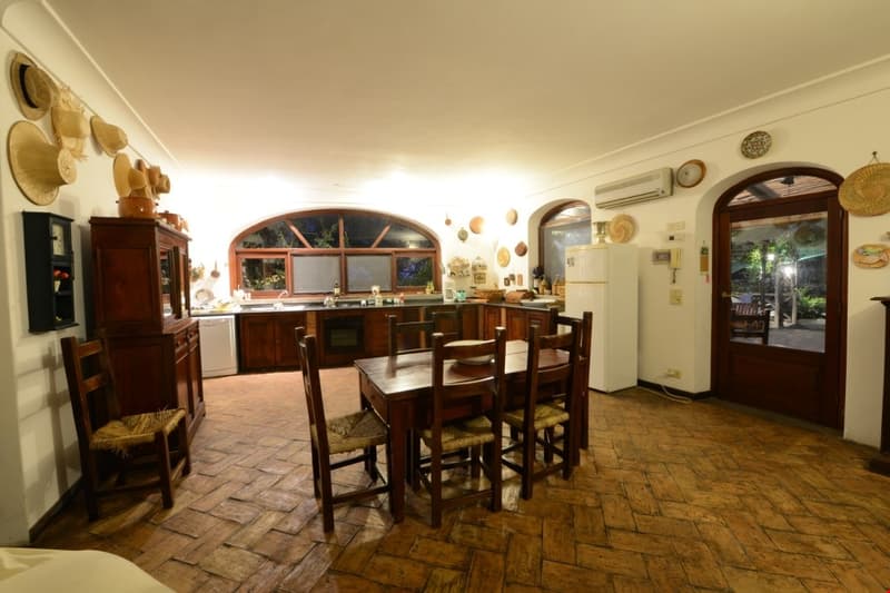 Spacious kitchen with wooden cabinets, arched window, dining table and chairs, tiled floor, and various kitchen appliances including a dishwasher