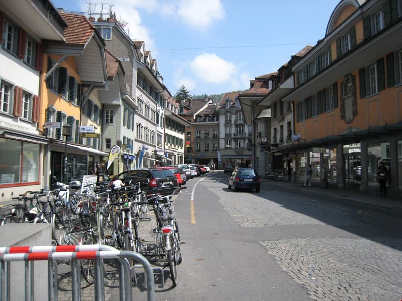 Cobblestone street lined with traditional European-style buildings, parked cars, and a row of bicycles along the sidewalk