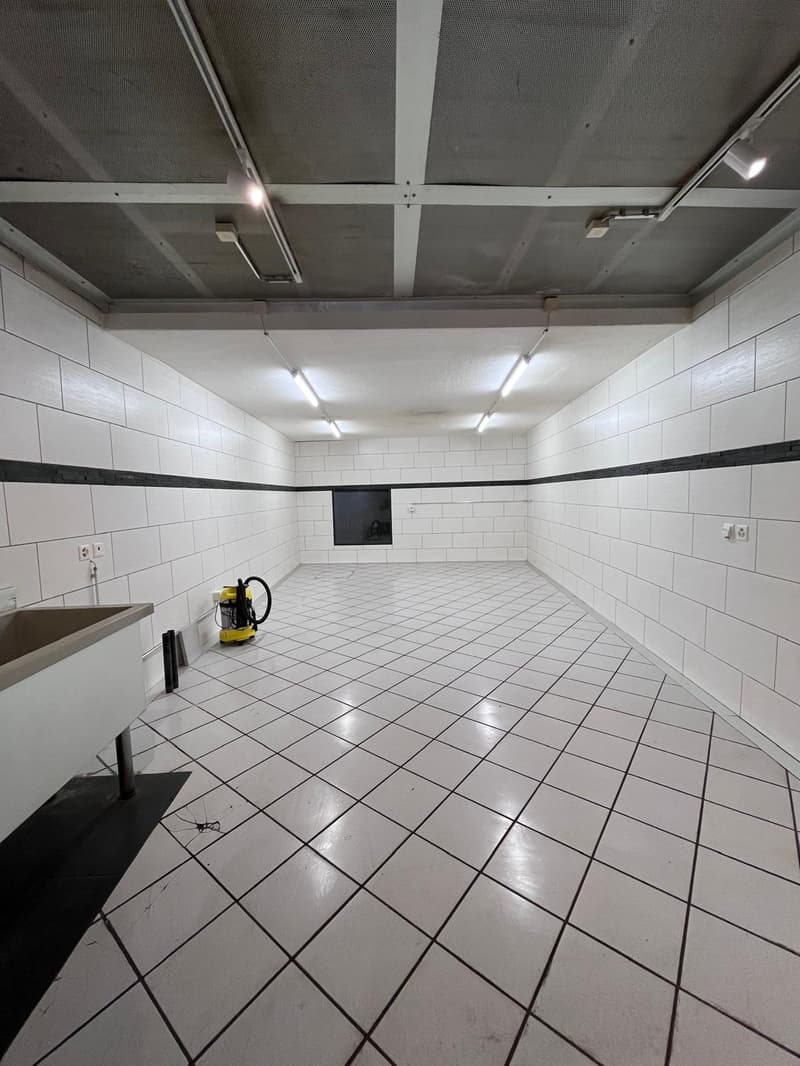 Empty room with white tiled floor, white walls, black trim, ceiling lights, sink, and a yellow vacuum cleaner