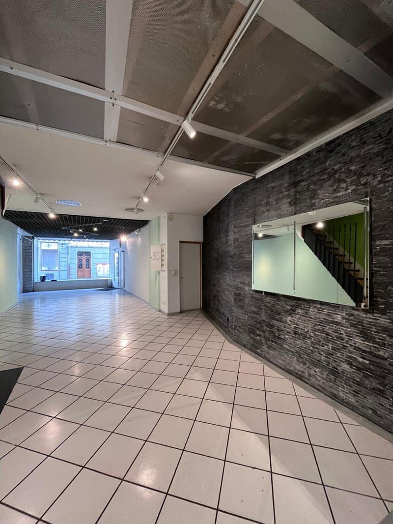 Empty room with white tiles, brick wall, large mirror, and a staircase visible in the mirror.