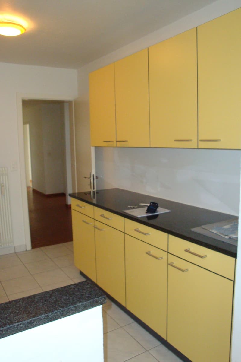 modern kitchen with yellow cabinets, black countertops, granite countertop, white tiles, ceiling light