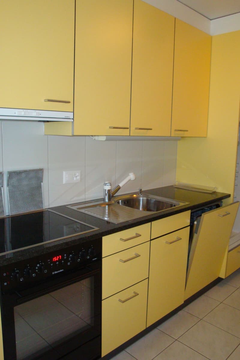 yellow cabinets, black countertops, stainless steel sink, electric stove, dishwasher, power outlet, digital clock on oven