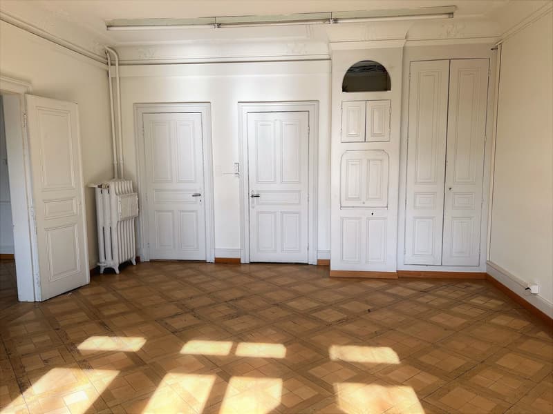 Empty room with wooden floors, four white doors, a white radiator, and white walls.