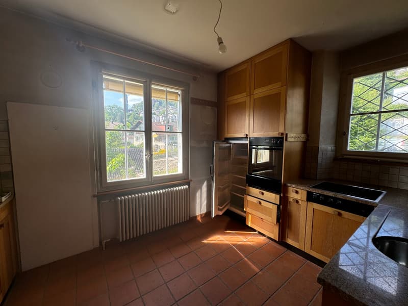 Kitchen with large windows, tile flooring, white radiator, white refrigerator, oven, black stovetop, kitchen cabinets, granite countertop, sink.