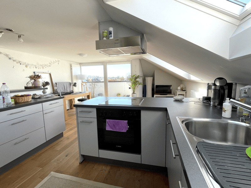 modern kitchen with wooden floor, white cabinets, black countertops, stainless steel sink, black oven, stainless steel range hood, large windows, skylight