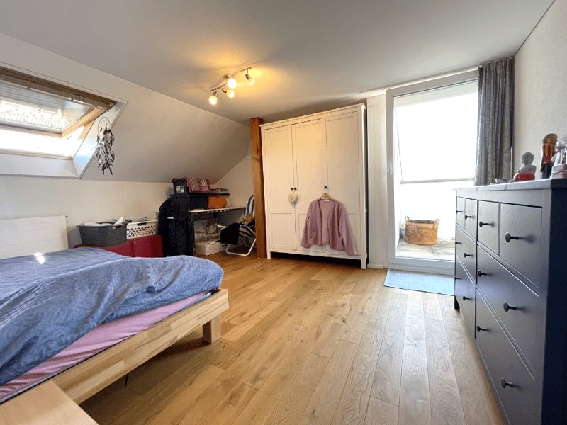 bedroom with bed, wooden floor, white wardrobe, pink sweater hanging, wooden desk, red storage boxes, skylight, ceiling lights, rug, drawers