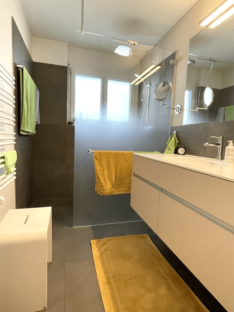 modern bathroom with glass shower, white sink, yellow towels, white radiator, yellow rug