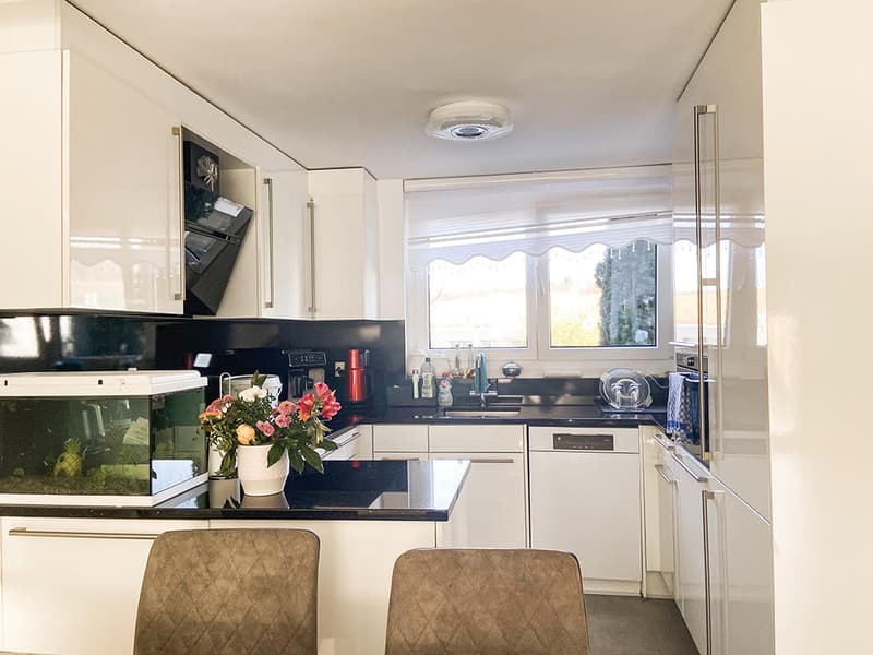 modern kitchen with white cabinets, black countertops, white appliances, flower vase, fish tank, window with blinds