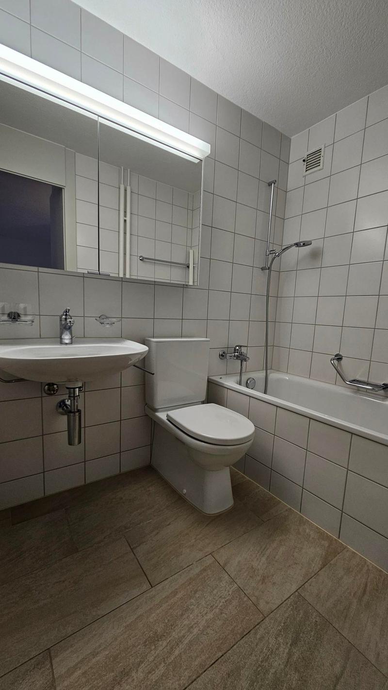 Bathroom with white tiles, wooden floor, white sink, white toilet, bathtub with shower, mirror
