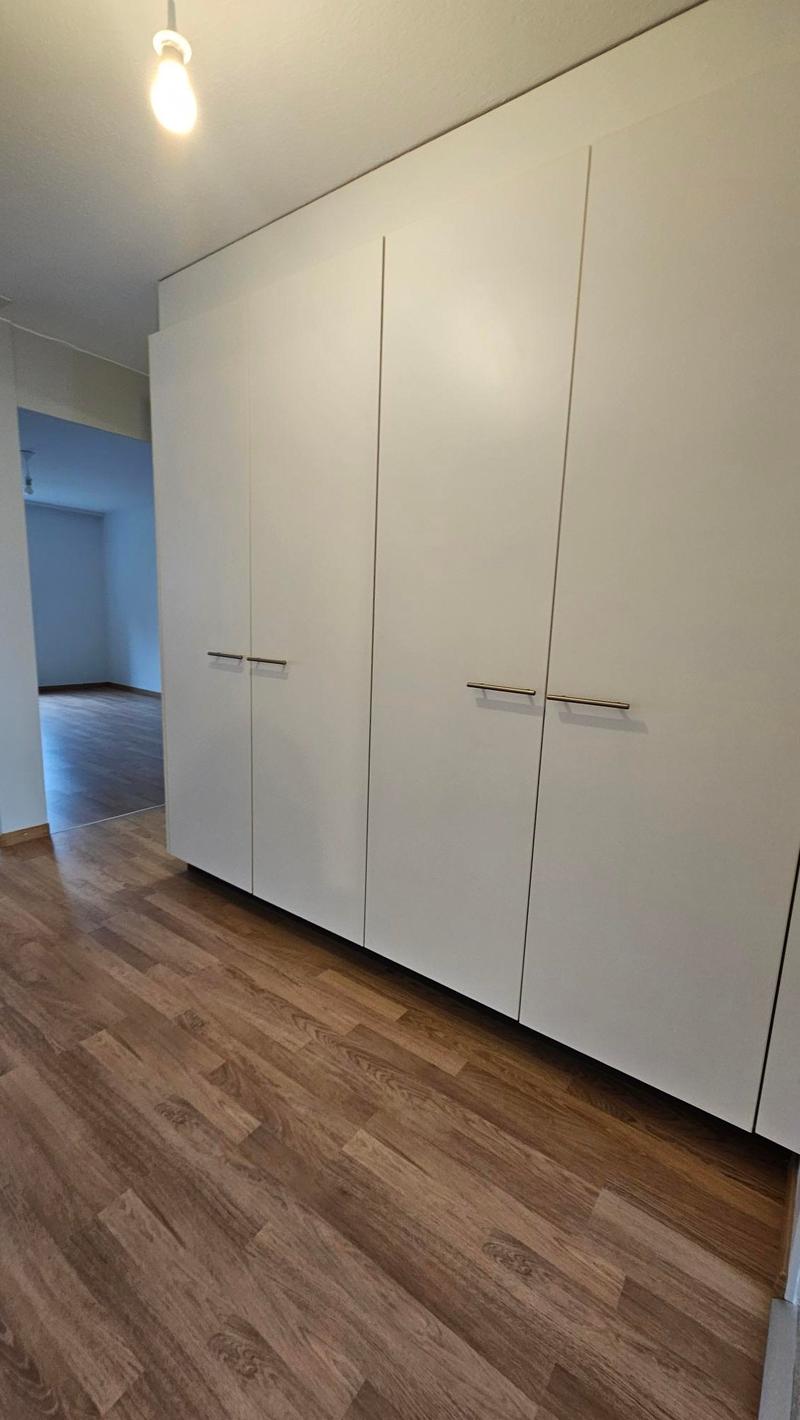 Empty room with wooden floor, white walls, large white wardrobes, and a ceiling light