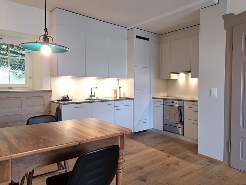 modern kitchen with wooden table, white cabinets, stainless steel appliances, wooden floor