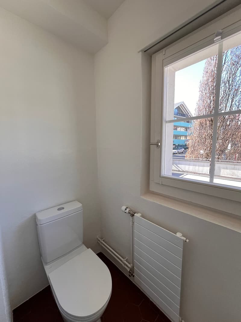A small bathroom with a toilet, radiator, and window