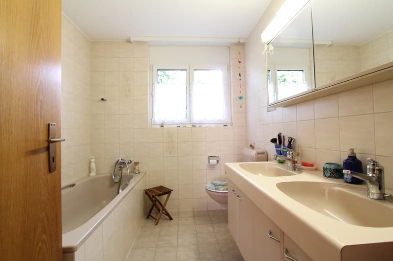 Bathroom with bathtub, two sinks, mirror, toilet, wooden stool, and window with curtains