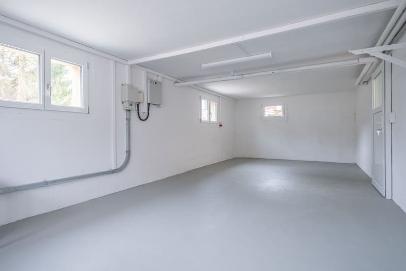 Empty room, white walls, gray floor, three windows, pipes on the wall, door