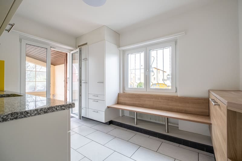 modern kitchen with white tiles, wooden bench, white cabinets, granite countertop, glass door, window with grills
