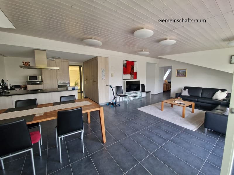 Modern interior with grey tiled flooring, open kitchen with wooden cabinets, dining table, living room with couch, television, and coffee table. A white rug covers part of the floor. The image also includes several round ceiling lights.