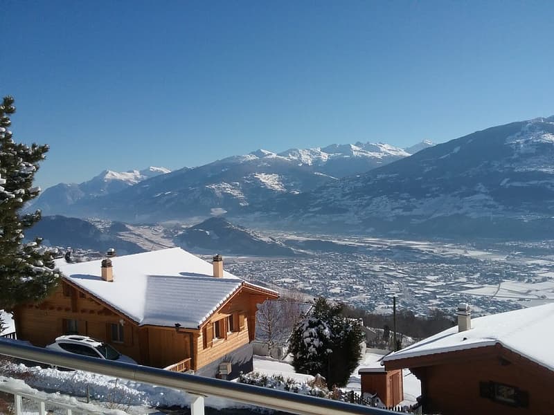 2 story chalet, wooden facade, snow covered roof, parked car, snowy landscape, mountain view
