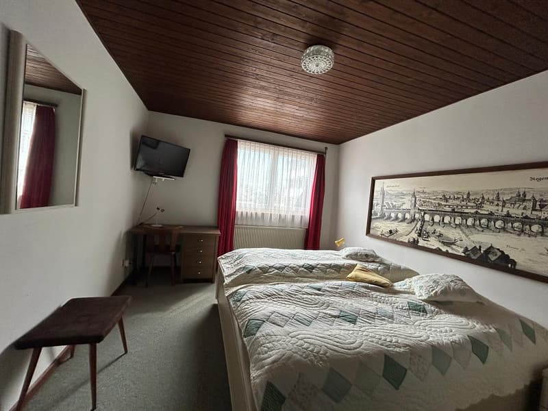 Cozy bedroom with wooden ceiling, large window, TV, dresser, and artwork on the wall