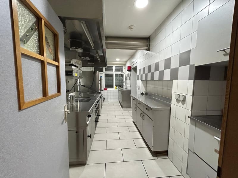 Galley-style kitchen with white and black tile flooring, stainless steel appliances including a stove and dishwasher, and wooden framed wall decor
