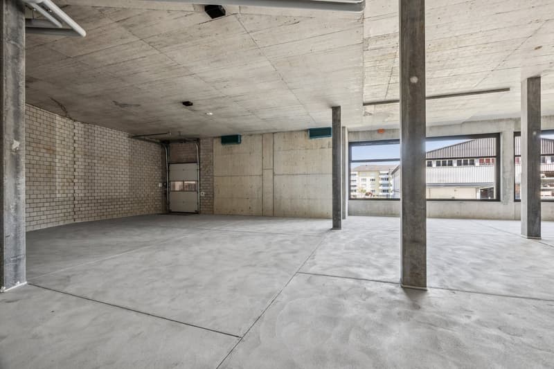 Large open space with concrete floor, exposed ceiling, and brick walls. The space appears to be a garage or storage area with a garage door visible.