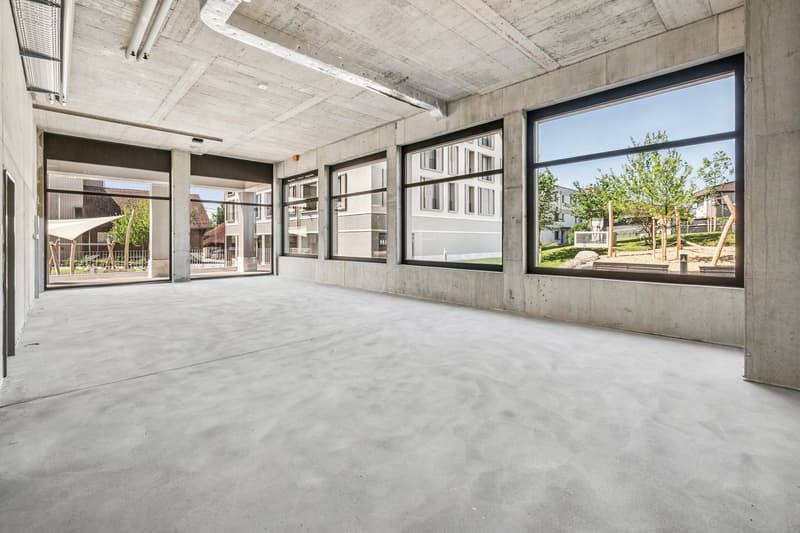 Large open space with concrete floors, high ceilings, and large windows overlooking a green outdoor area