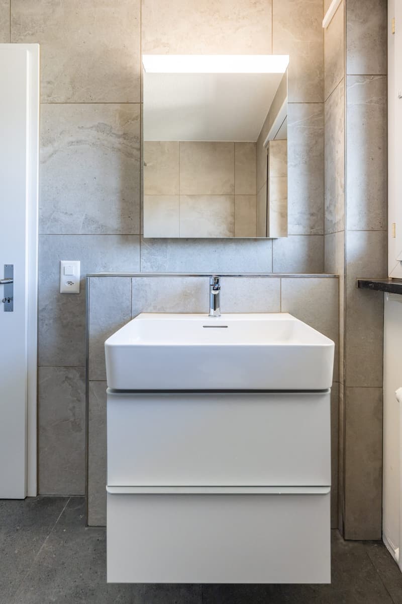 Bathroom with white sink, mirror, and tiled walls
