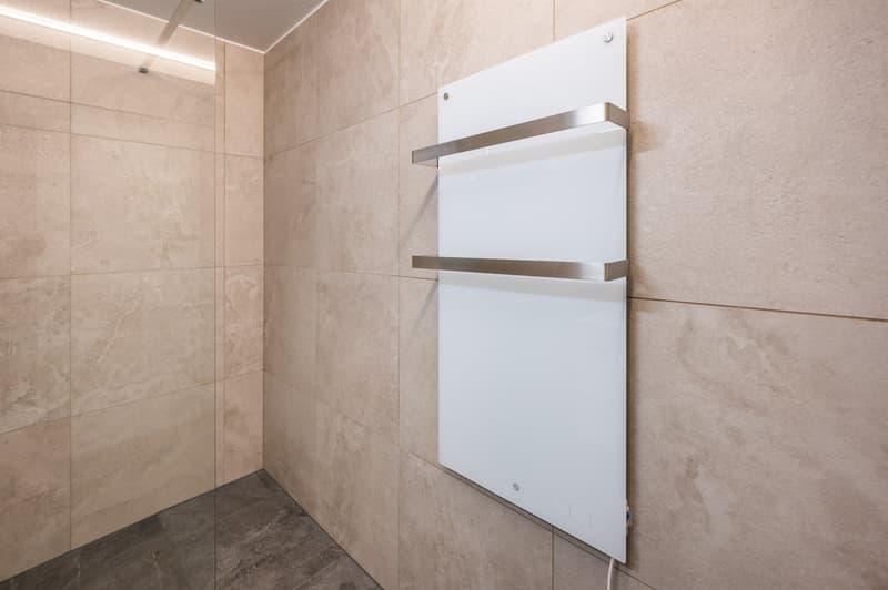 Bathroom with tiled walls, glass shower enclosure, white wall-mounted towel warmer, and a power outlet.
