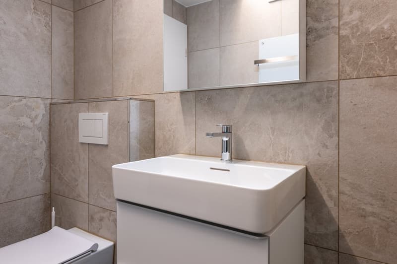 Bathroom with a white sink, mirror, and tiled walls