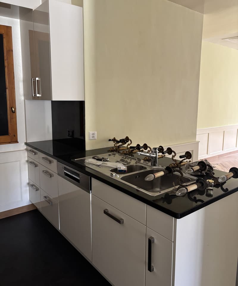 modern kitchen, white cabinets, black countertops, stainless steel sinks, dishwasher, gas stove, wooden floor, power outlets