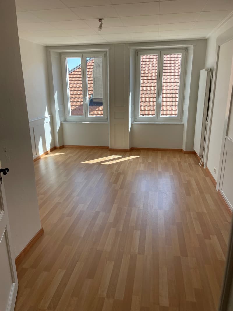 Wooden floor, two windows with red roofs visible, white walls