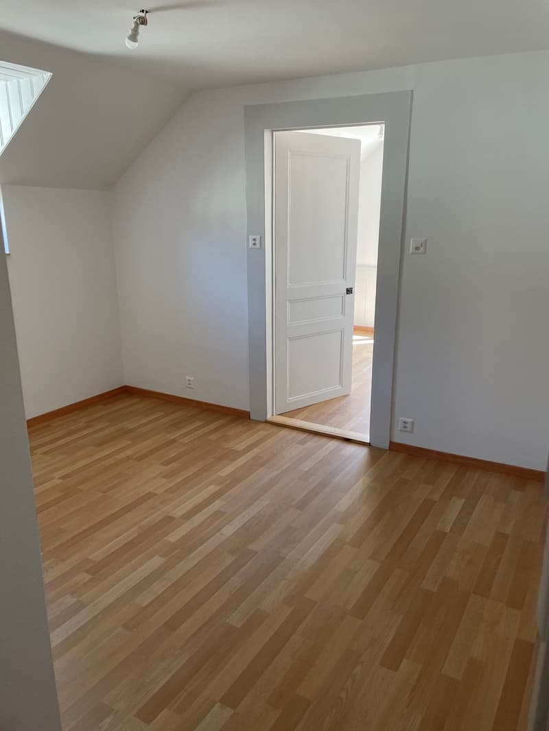 Empty room with white walls and wooden floor, open door leading to another room