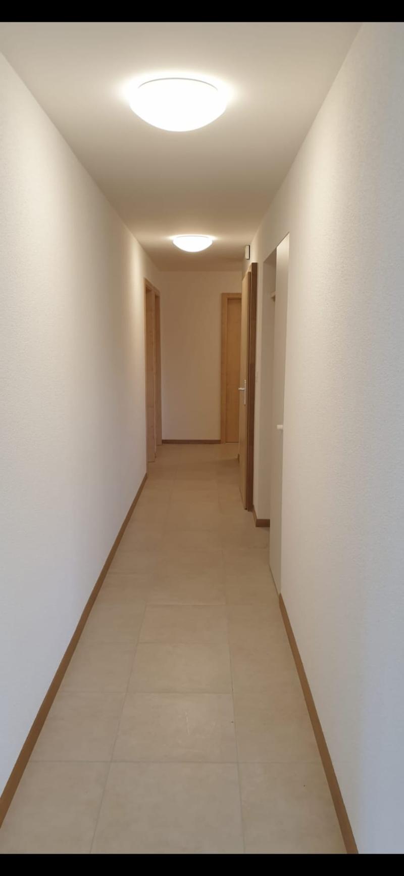 Empty hallway, tiled floor, white walls, ceiling lights, closed doors