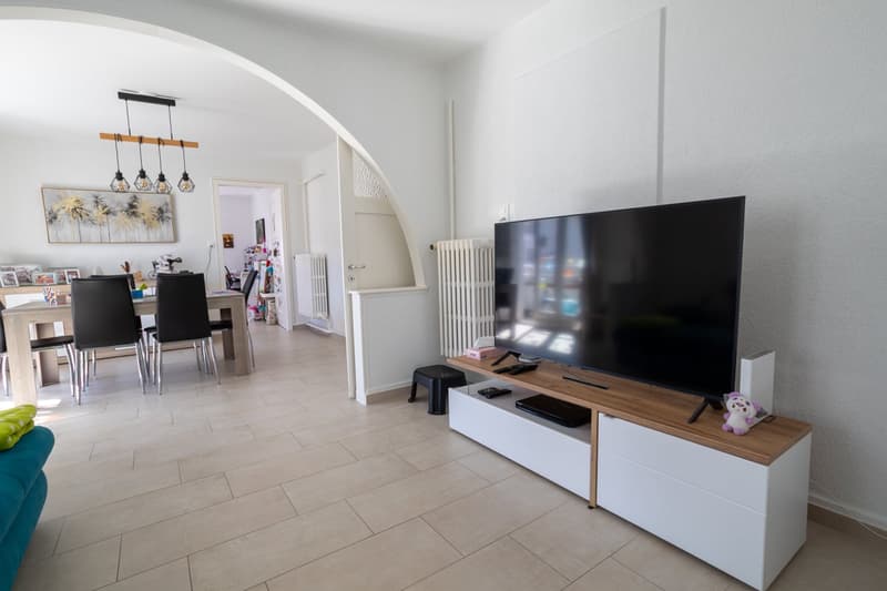 Living room with a flat screen TV, a wooden entertainment center, a dining table with chairs, a radiator, and a chandelier.