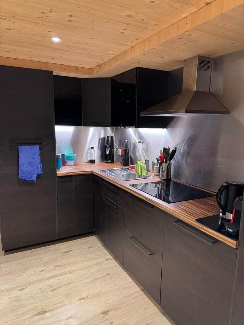 modern kitchen, wooden countertops, black cabinets, stainless steel appliances, gas stove, electric kettle, coffee maker, wooden flooring, ceiling lamps