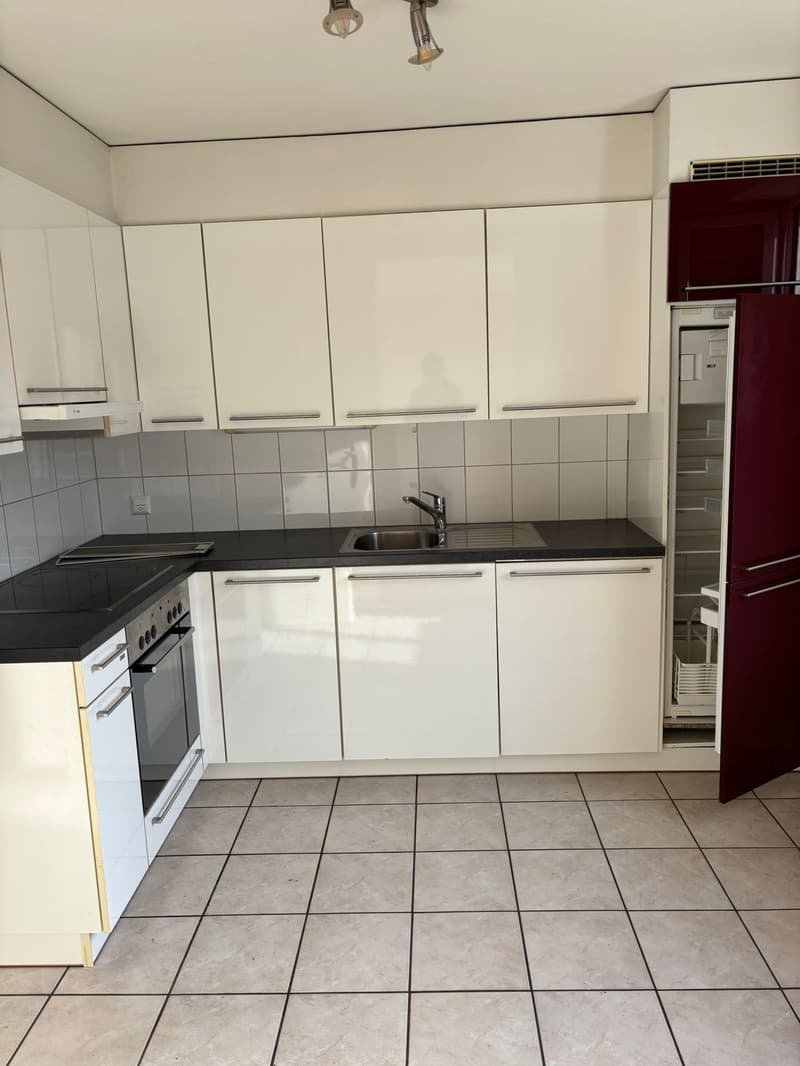 Modern kitchen with white cabinets, black countertops, stainless steel sink, and a red refrigerator.