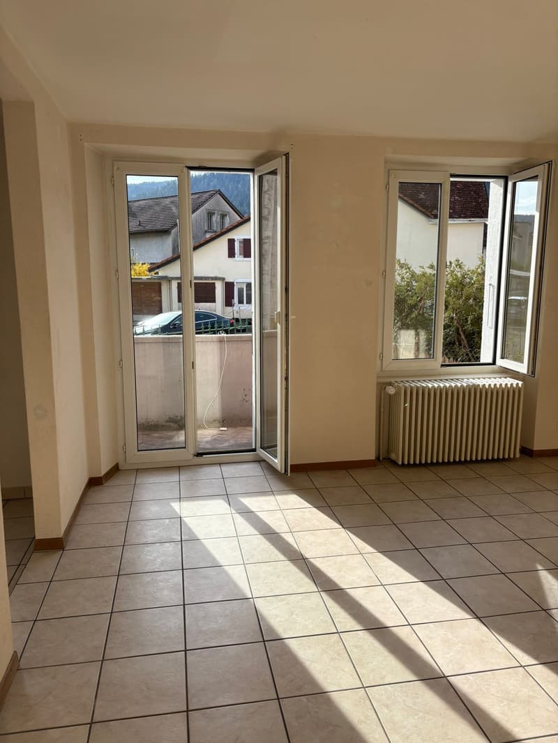 Empty room with white tiles, glass doors, and windows. A radiator is present on the wall.
