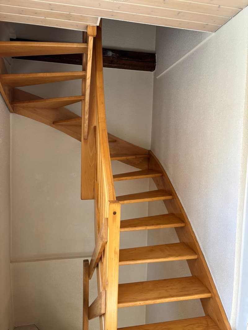 A wooden spiral staircase with a white wall on the side.