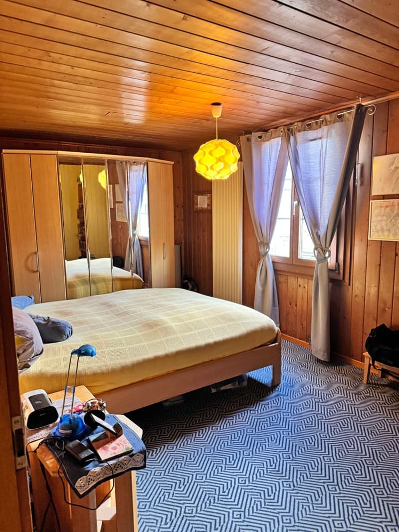 bedroom with wooden walls, bed, lamp, nightstand, mirror, window, curtains, wooden floor, wooden cabinet