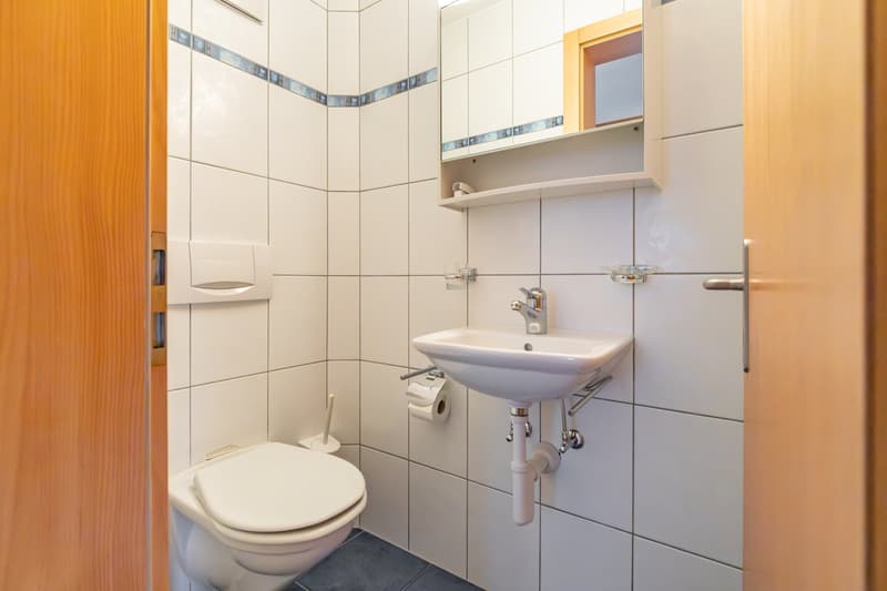 Small bathroom with white tiles, a toilet, a sink, and a mirror