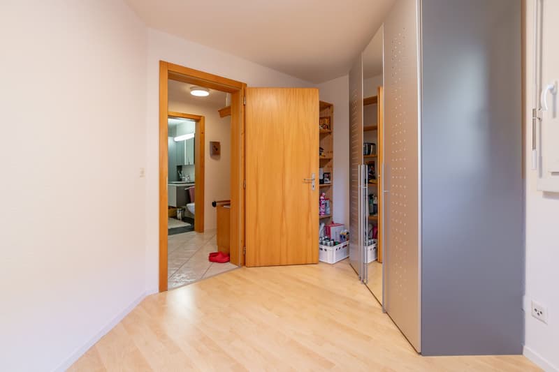 empty corridor, wooden flooring, shelves, mirror, open doors to bathroom and another room